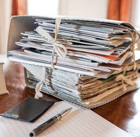 Stack of photo albums bound together with a pen and notebook on a wooden surface