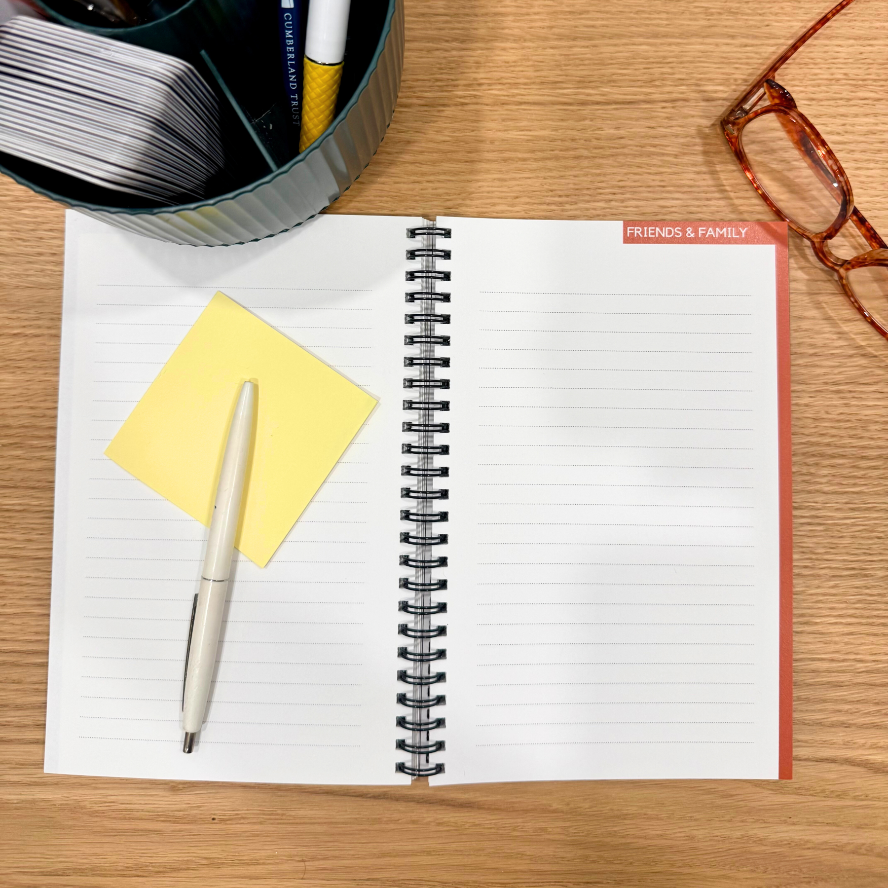 Open notebook with pen, sticky notes, and stationery items on a wooden desk